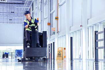 A Leadec employee cleaning the floor at a factory with a cleaning machine.