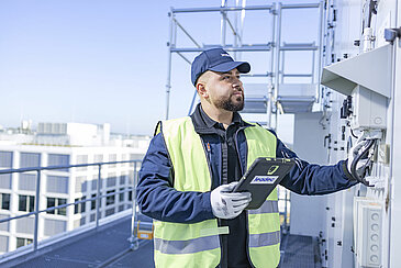 Leadec employee with a tablet on a factory roof checks external installation of ventilation system.