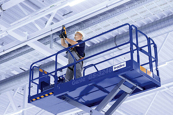 Leadec employee on a scissor lift installing media supply on the ceiling of a factory.